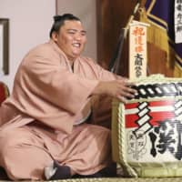 Autumn Grand Sumo Tournament champion Mitakeumi poses with a cask of sake on Monday at Dewanoumi stable in Sumida Ward. | KYODO
