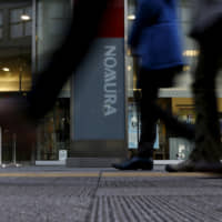 edestrians walk past a signboard of Nomura Securities outside its branch in Tokyo in 2016. | REUTERS