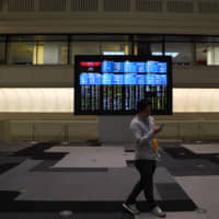 A man walks in front of a screen displaying share prices inside the Tokyo Stock Exchange in May. | BLOOMBERG