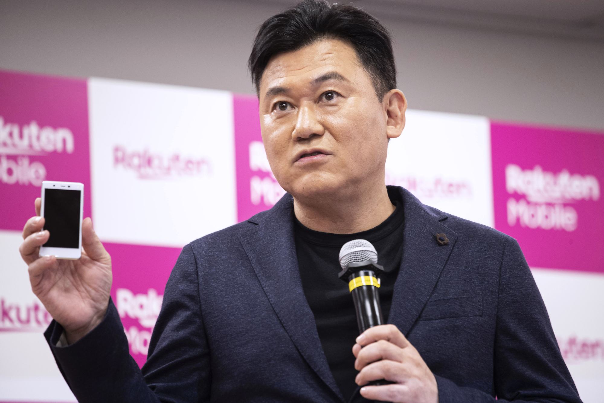 Hiroshi Mikitani, chairman and chief executive officer of Rakuten Inc., displays a Rakuten Mini smartphone during a news conference in Tokyo in September. | BLOOMBERG