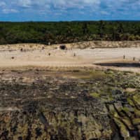 A drone view shows volunteers removing crude oil spilled at the Pocas beach, municipality of Conde, Bahia state, Brazil, Sunday. Large blobs of oil staining more than 130 beaches in northeastern Brazil began appearing in early September and have now turned up along a 2,000-km stretch of the Atlantic coastline. The source of the patches remains a mystery despite President Jair Bolsonaro\'s assertions they came from outside the country and were possibly the work of criminals. | AFP-JIJI