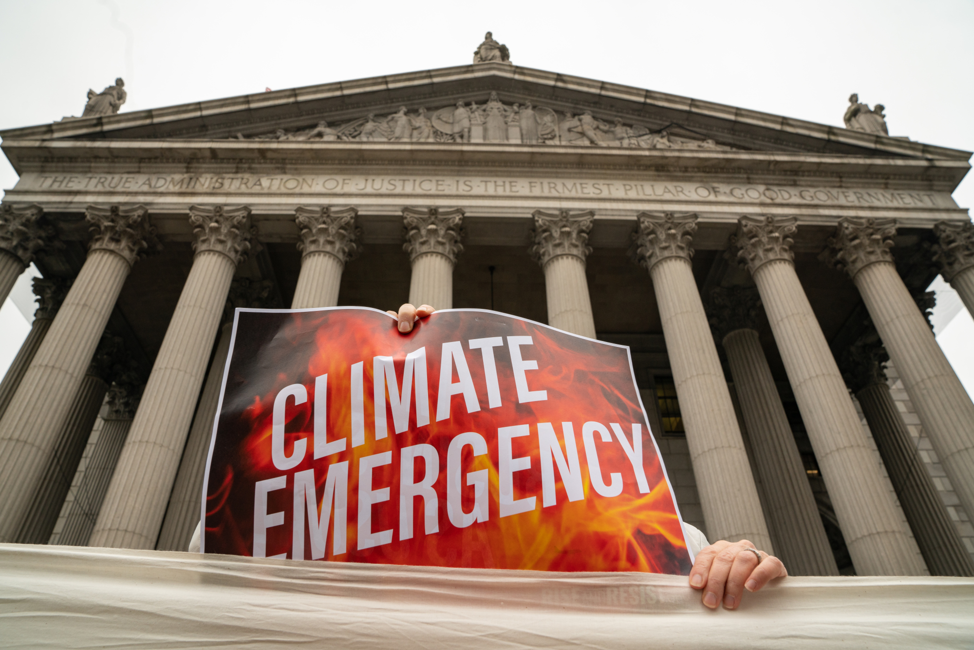 A demonstrator holds a sign at a protest on the first day of the ExxonMobil Corp. trial outside the New York State Supreme Court building on Tuesday. | BLOOMBERG