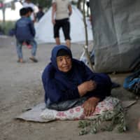 A woman rests next to her tent at a makeshift camp for refugees and migrants next to the Moria camp on the island of Lesbos, Greece, Wednesday. | REUTERS