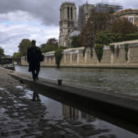 A man walks along the side of the River Seine near Notre Dame Cathedral in Paris on Wednesday. | AP