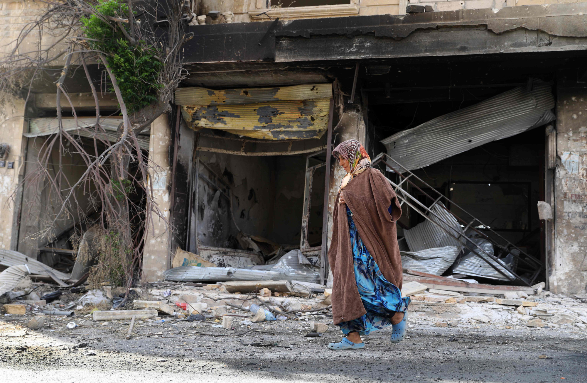 A woman passes shops damaged in attacks by pro-regime forces in the Syrian village of Kafr Nabl, in southern Idlib province, on Sunday. | AFP-JIJI