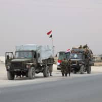 A convoy transporting Syrian troops stand on the outskirts of the northern Syrian border town of Kobani on Wednesday. | AFP-JIJI