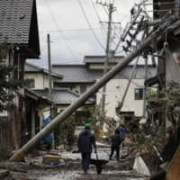 Residents walk along a mud-covered road in a neighborhood in Nagano Prefecture that was devastated by Typhoon Hagibis on Oct. 15. | AP