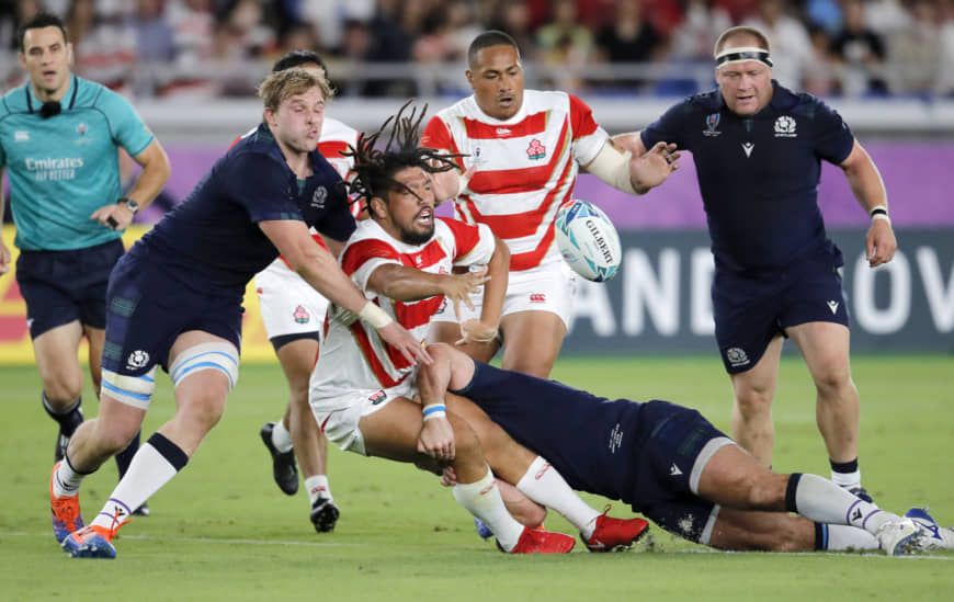 Japan's Shota Horie passes the ball as he is tackled during Sunday night's match. | AP