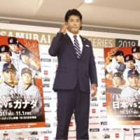 Japan manager Atsunori Inaba on Tuesday stands next to promotional posters for upcoming warmup games against Canada in Okinawa before the Premier12 tournament. | KYODO