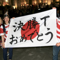 Japan supporters outside International Stadium Yokohama hold up a flag reading \'Congratulations on reaching the knockout tournament\' after Japan\'s Pool A win over Scotland on Sunday night. | KAZ NAGATSUKA