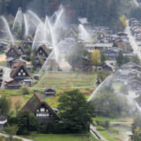 Firefighters and local residents discharge water over traditional wooden houses in Shirakawa-go, Gifu Prefecture, on Sunday during an annual fire drill. The 114 houses, built in the high-roof gasshō-zukuri style, are registered as UNESCO Cultural Heritage sites and are a popular tourist attraction. | KYODO