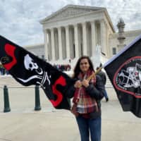 Christina Burnham holds pirate-themed flags in front of the Supreme Court in Washington NTuesday in support of her uncle, Frederick Allen, a filmmaker whose appeal in a copyright lawsuit over the use of his footage of Blackbeard\'s shipwreck is being heard by the justices. | REUTERS