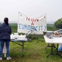 A woman stands at a collapsable table washing dishes during a rally to protest the construction of the EuropaCity Commercial and Leisure Mall project in Gonesse near Paris last May. France\'s president announced that the controversial Europacity project will be discarded, AFP reported Thursday. | AFP-JIJI