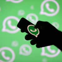 A man poses with a smartphone in front of a displayed Whatsapp logo in this 2017 illustration. | REUTERS