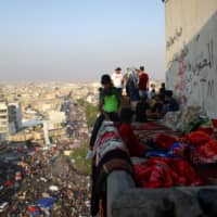 Iraqi demonstrators sit atop the Turkish Restaurant Building, during anti-government protests in Baghdad on Saturday. | REUTERS