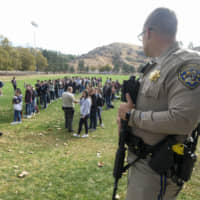 A police officer stands guard as students wait to be reunited with their parents following a shooting at Saugus High School that injured several people, Thursday in Santa Clarita, California. | AP