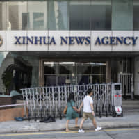 Pedestrians walk past a vandalized entrance to the offices of China\'s state-run Xinhua News Agency  in Hong Kong on Sunday, a day after protesters went on the rampage and vandalized the offices and some other buildings. | BLOOMBERG