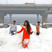 People pose as they stand amid the foam covering the polluted Yamuna river on a smoggy morning in New Delhi Sunday. | REUTERS