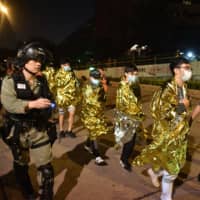 Unwell and injured protesters, wrapped in emergency thermal blankets, leave the campus of Hong Kong Polytechnic University on Tuesday. | AFP-JIJI