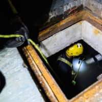 A rescue diver enters a sewer to search for anti-government protesters who tried to escape from the besieged Hong Kong Polytechnic University (PolyU) after being barricaded inside for days, in the Hung Hom district of Hong Kong Tuesday. | AFP-JIJI