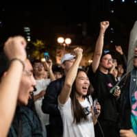Pro-democracy supporters chant as they celebrate after pro-Beijing candidate Junius Ho lost a seat in the district council elections in the Tuen Mun district of Hong Kong, early on Monday. Hong Kong\'s voters turned out in record numbers for local council elections that the city\'s pro-democracy movement hopes will add pressure on the Beijing-backed government to heed their demands after months of violent protest. | AFP-JIJI
