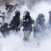 Police in riot gear move through a cloud of smoke as they detain a protester at Hong Kong Polytechnic University in the city on Monday. | AP
