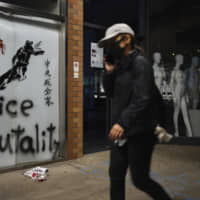 A protester walks past graffiti depicting police as a dog and various slogans including \"Hongkongers Resist, \"Chinese Communist whole family die\" at the Hong Kong Polytechnic University in Hong Kong on Wednesday. A small band of anti-government protesters, their numbers diminished by surrenders and failed escape attempts, remained holed up at the Hong Kong university early Wednesday as they braced for the endgame in a police siege of the campus. | AP