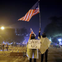 Protesters hold British and American flags and a sign reading \"Save Us\" as they stand near Hong Kong Polytechnic University on Sunday. | AP