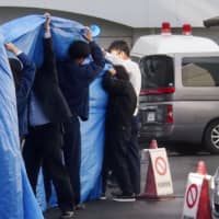 Officials cover a vehicle transporting a 14-year-old boy accused of attempted murder from Hachinoe Police Station in Aomori Prefecture on Thursday. | KYODO