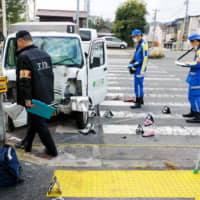Police officers conduct an investigation at a crossing in Hachioji, in western Tokyo, on Monday morning after a vehicle crashed into a group of nursery school children and teachers. Six of them were injured, as well as the driver. | KYODO