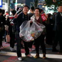 Yuki Satake (left) and Masaki Takuma pick up trash in Shibuya during Halloween festivities on Thursday night. | RYUSEI TAKAHASHI