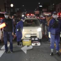 Police officers stand guard on Wednesday on a street in Kyoto where a gang member was arrested over the fatal shooting of a rival group member in Amagasaki, Hyogo Prefecture. | KYODO