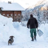 A man clears snow around a house on Monday after heavy snowfalls in Kals am Grossglockner, Austria. | AFP-JIJI