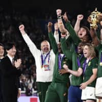 Prime Minister Shinzo Abe (far left) and Crown Prince Akishino (second from left) applaud as South Africa\'s flanker Siya Kolisi lifts the Webb Ellis Cup as the team celebrates winning the 2019 Rugby World Cup final match against England at the International Stadium Yokohama in the city on Saturday. | AFP-JIJI