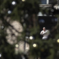 Pope Francis, framed by a St. Peter\'s Square Christmas tree, waves during the Angelus noon prayer he recited from the window of his studio, at the Vatican Sunday. | AP
