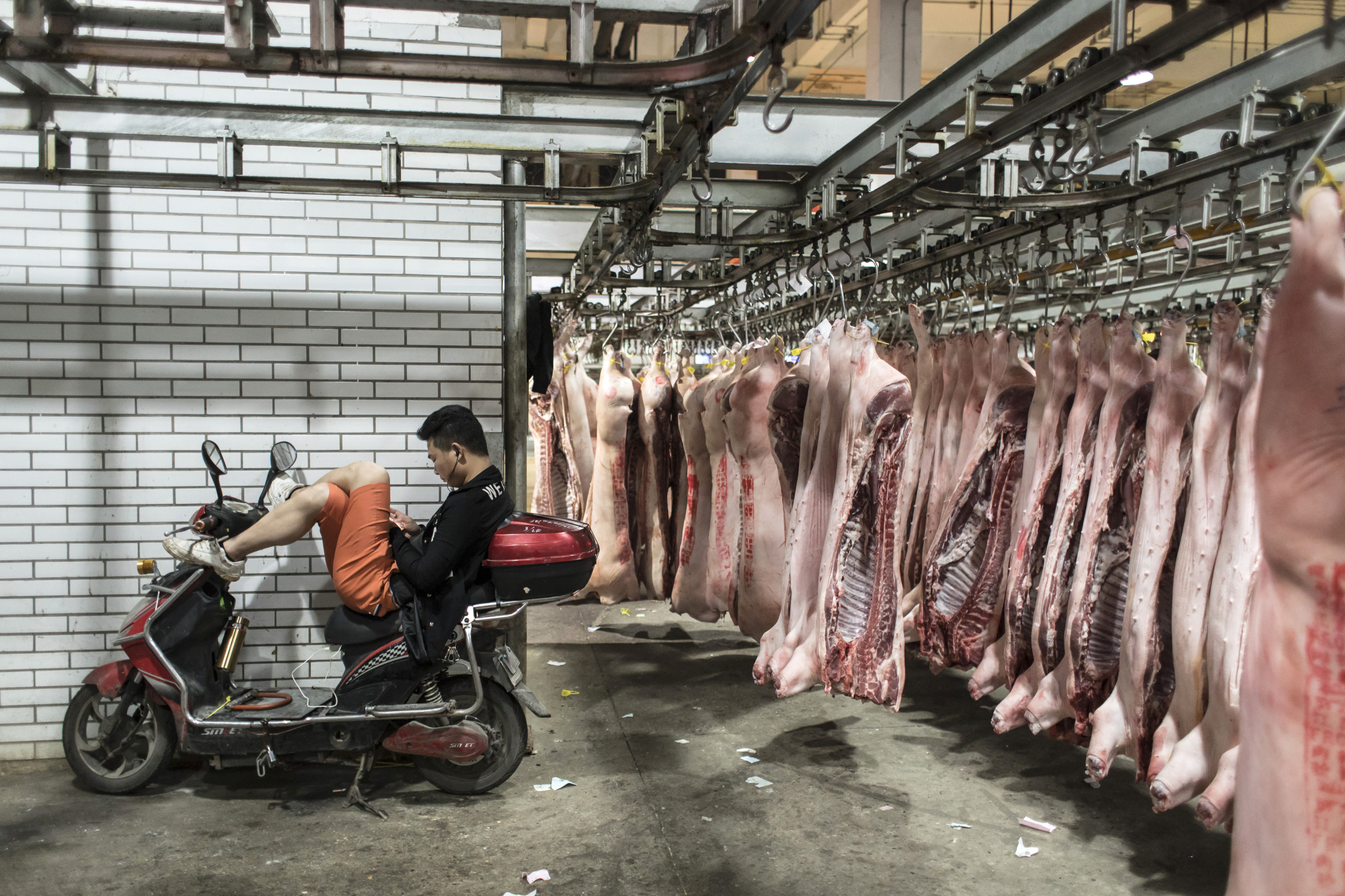 A man sits on a motorcycle at a pork wholesale market on the outskirts of Shanghai. China has cut import tariffs on a wide range of goods including pork, consumer and technology items. | BLOOMBERG