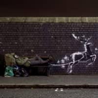 A man lies on a bench next to a new mural by Banksy in Birmingham, England, on Monday. | @BANKSY VIA REUTERS