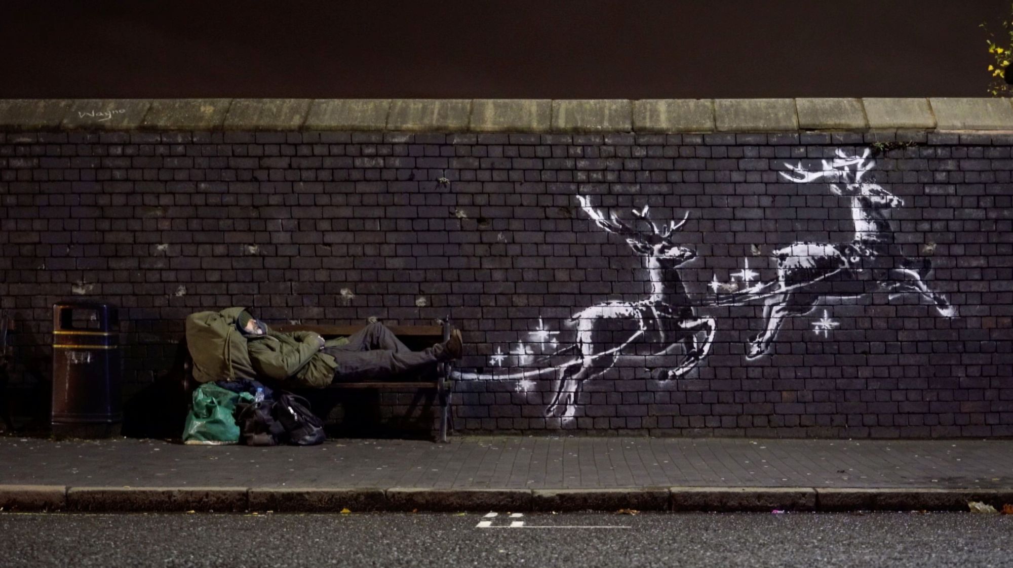 A man lies on a bench next to a new mural by Banksy in Birmingham, England, on Monday. | @BANKSY VIA REUTERS