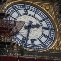 A worker stands on a scaffolding platform near one of the four clock faces on the Elizabeth Tower, also known as Big Ben, at the Houses of Parliament in London in April. The bell in the landmark tower, whose restoration work is due to be completed in 2021, will ring at midnight on New Year\'s Eve. | BLOOMBERG