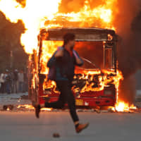A man runs past a burning bus that was set on fire by demonstrators during a protest against a new citizenship law in New Delhi on Sunday. | REUTERS