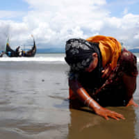 An exhausted Rohingya refugee woman touches the shore in Shah Porir Dwip, Bangladesh, in September 2017 after crossing from Myanmar by boat through the Bay of Bengal. | REUTERS