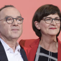 Norbert Walter-Borjans and Saskia Esken stand on the podium after winning the Social Democratic Party chairmanship at the party\'s headquarters in Berlin on Saturday. | AP