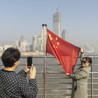 A passenger holds a Chinese flag while crossing the Yangtze River by ferry in Wuhan, China, on Dec. 11. | BLOOMBERG