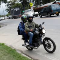 Anthony Vazquez from Venezuela sits on his motorcycle with a passenger on the outskirts of Bogota Saturday. | REUTERS