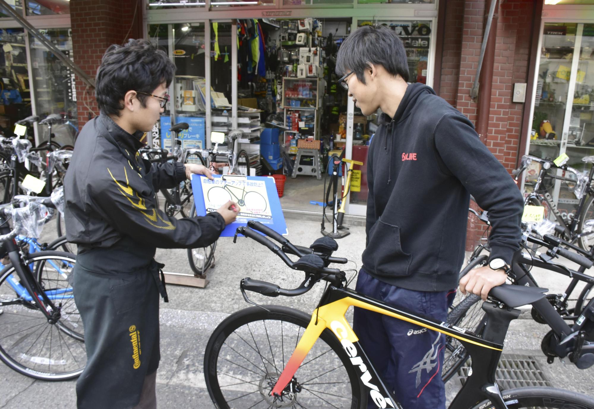 A clerk speaks with a customer about bicycle insurance at a bike shop in Kagoshima last month. | KYODO