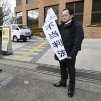 A plaintiff holds a banner that reads \"unfair ruling\" outside the Nagoya District Court on Friday, after losing a case against the state over the My Number identification system. | KYODO