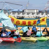 Protesters shout in canoes off Okinawa Saturday near the site of the new home for U.S. Marine Corps Air Station Futenma, a year after landfill work for the transfer began. | KYODO