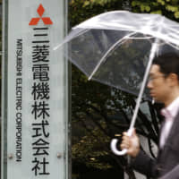 A man walks in front of a company signboard erected at the entrance of a building in Tokyo housing the headquarters of Mitsubishi Electric Corp. | KYODO