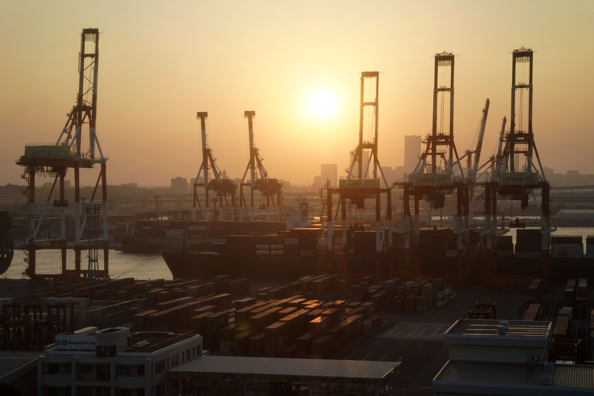 Stacked containers sit next to gantry cranes at a shipping terminal at dusk in Yokohama.  Japan prefers India's participation in the Regional Comprehensive Economic Partnership to avoid the creation of a China-led trading bloc. | BLOOMBERG