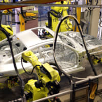 Four robots arms weld a Porsche 911 Coupe sports car body at a factory in Germany. | BLOOMBERG NEWS